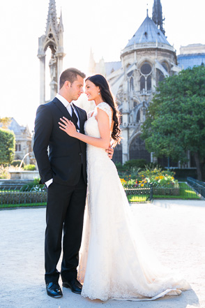Groom holds bride with sunset and Notre Dame in background