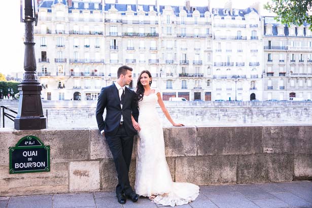 Bride and Groom Lean on Railing in Front of Paris Buildings