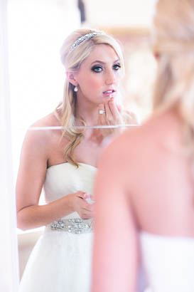 Bride Using Wall Mirror to Touch Up Lipstick