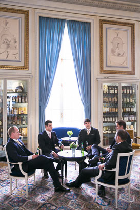 Groomsmen Sitting Around a Table in Front of Tall Window of a Chateau