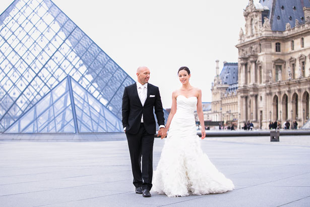 Bride and Groom Walk Past Louvre Pyramids in Paris